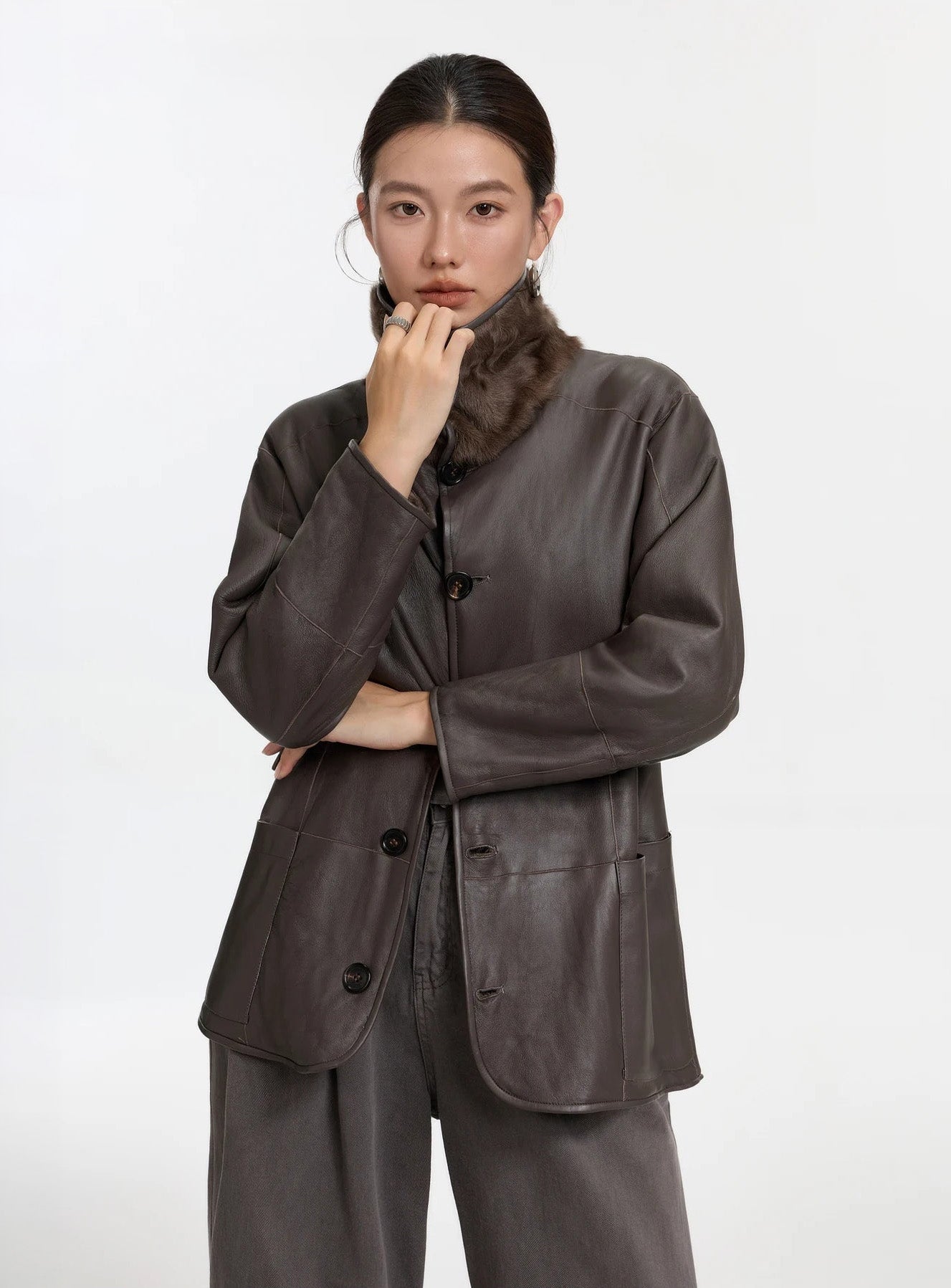 Model adjusting the fastened collar of the shearling coat, leather side visible, magnetic closure softly concealed — From Borcelleclothes.