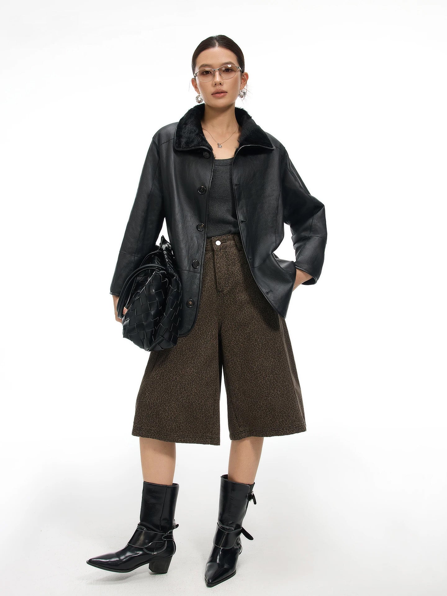 Model holding a bag while resting one hand on the hip, wearing the Tusch Swell coat leather side out — From Borcelleclothes.