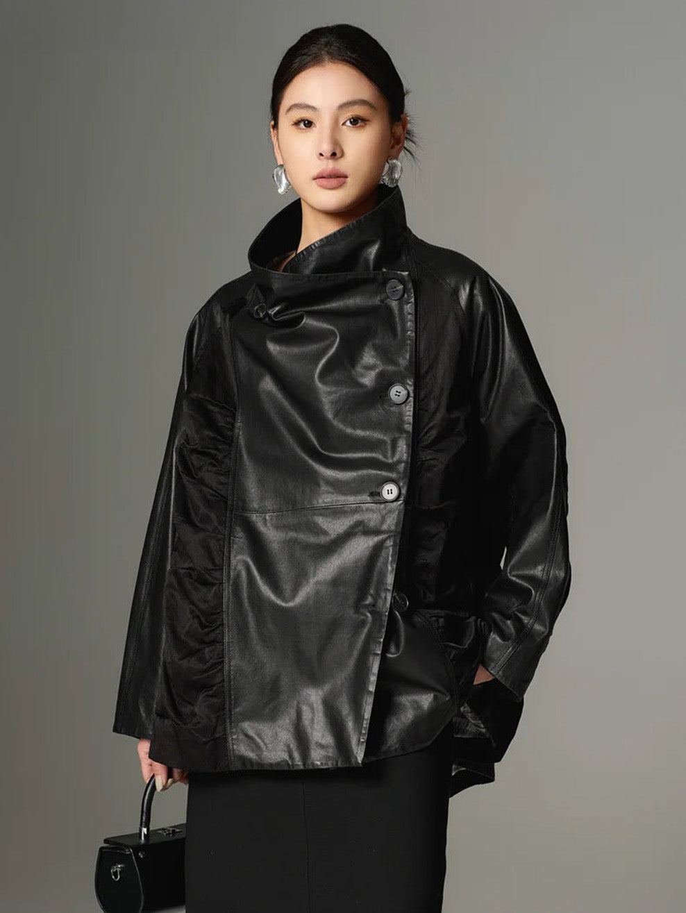 A close-up of the front panel drape in the Beneath the Mask jacket, showcasing the memory-wire-shaped folds as the model holds a black bag. — From Borcelleclothes.