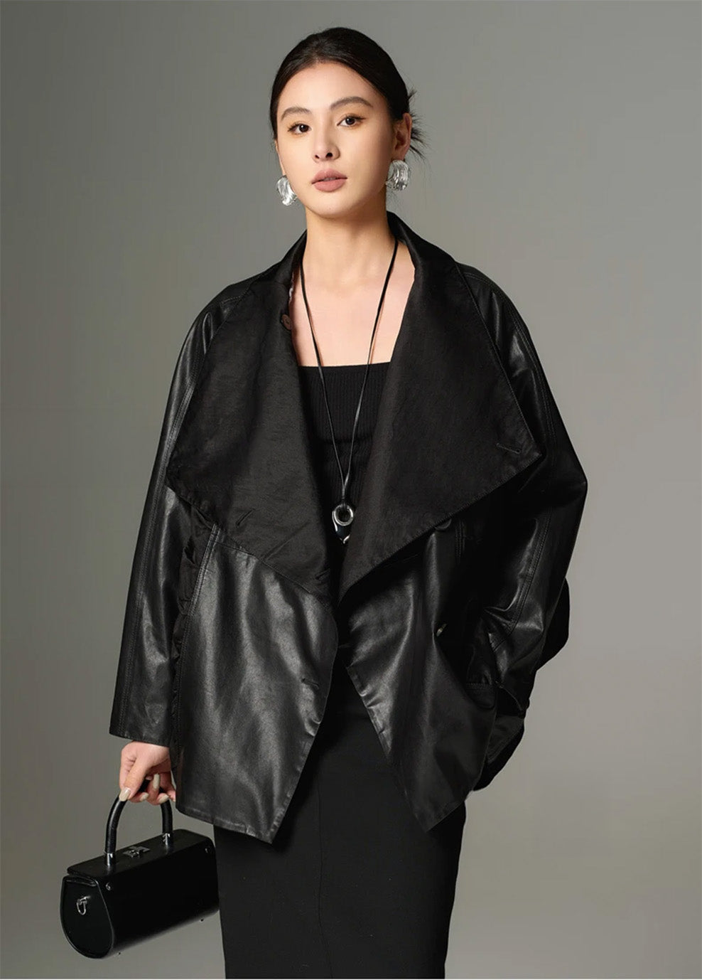 Model facing forward holding a black bag, with the deep matte collar unfastened to showcase the contrast with the substantial leather. — From Borcelleclothes.