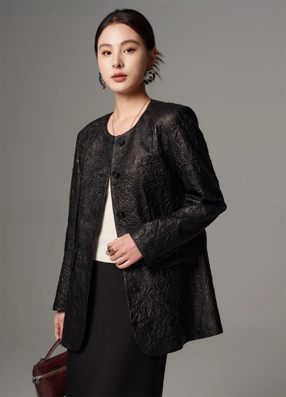 Detail pose of a model holding the front edge of an open crinkled sheepskin jacket — From Borcelleclothes.