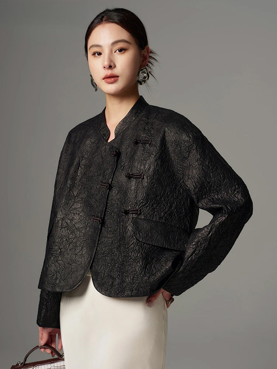 Three-quarter side angle of the model with a hand on her hip, displaying the profile of the cropped crinkled sheepskin wrap jacket in Frost-Glazed Lava — From Borcelleclothes.