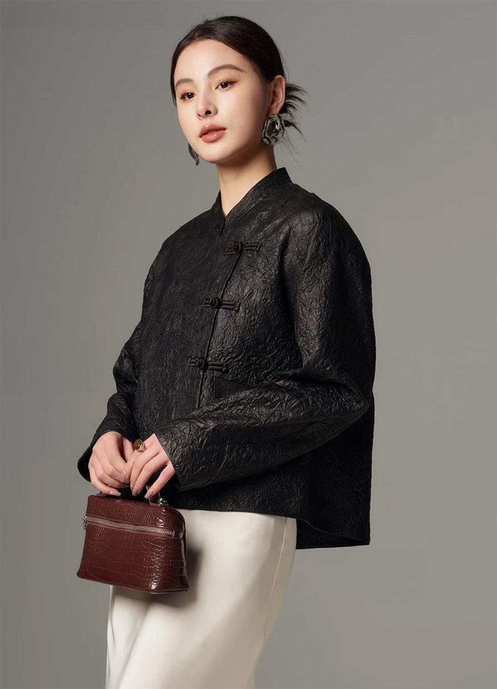 Full-length shot of the model holding a structured bag with both hands, wearing the Frost-Glazed Lava crinkled sheepskin pankou jacket — From Borcelleclothes.