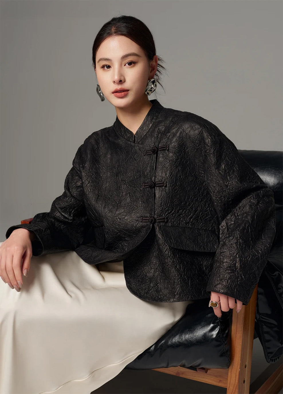 Model seated on a chair showcasing the natural drape, supple folds, and high-low hem of the crinkled sheepskin jacket in Frost-Glazed Lava — From Borcelleclothes.