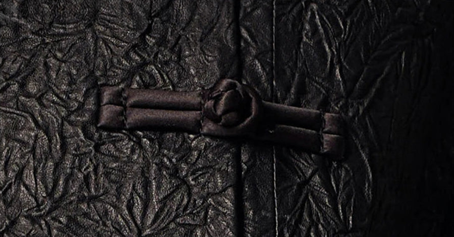 Macro focus on the handcrafted satin knot pankou closure and matching rouleau loop against the Frost-Glazed Lava crinkled sheepskin — From Borcelleclothes.