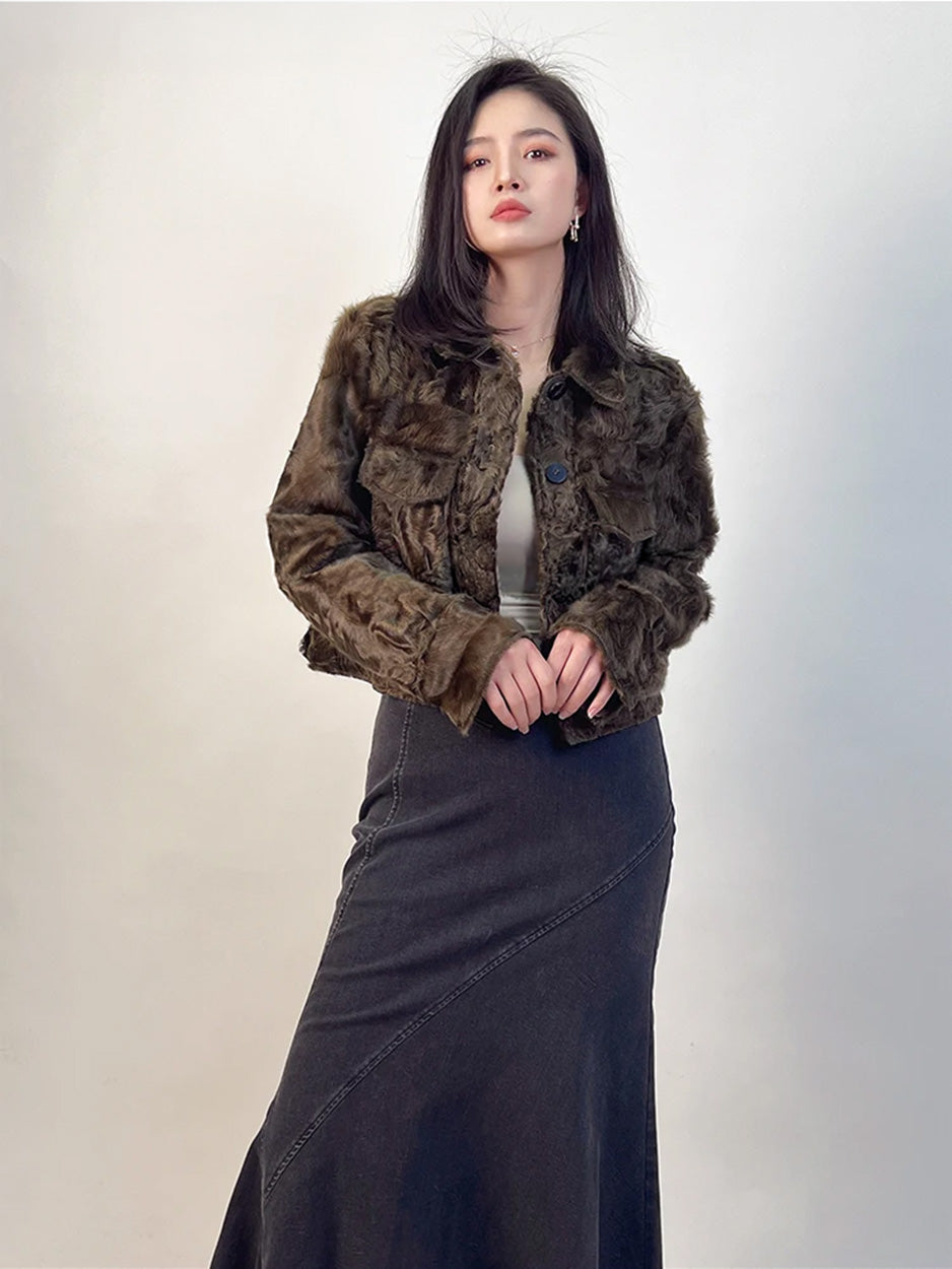 A close-up of the cropped shearling jacket as fingers gently touch, highlighting the contrast between the rigid structure and the shimmering fine-wool fleece. — From Borcelleclothes.