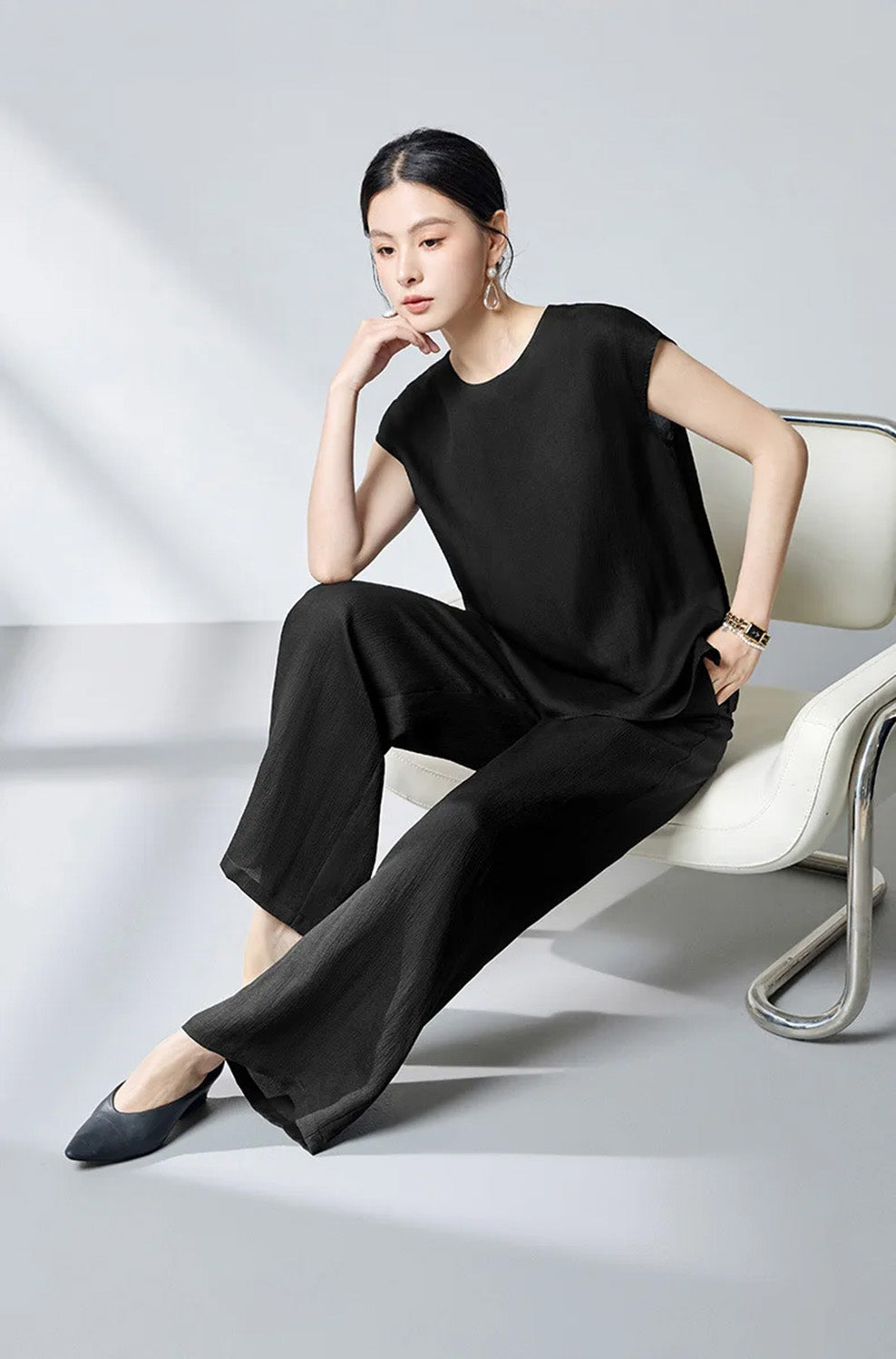 Model sitting in an armchair wearing the women's defined waist mulberry silk blouse in Queen of Spades — From Borcelleclothes.