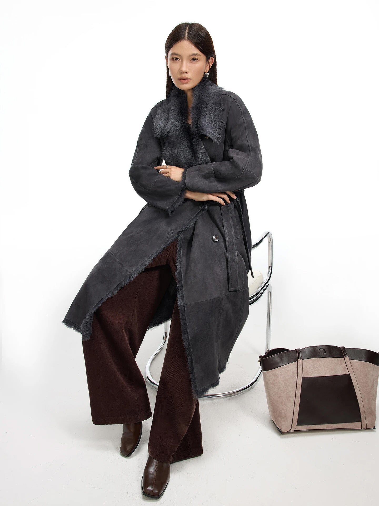 Model seated in the Enigma goatskin coat, highlighting the relaxed drape and suede texture of the wrap silhouette. — From Borcelleclothes.