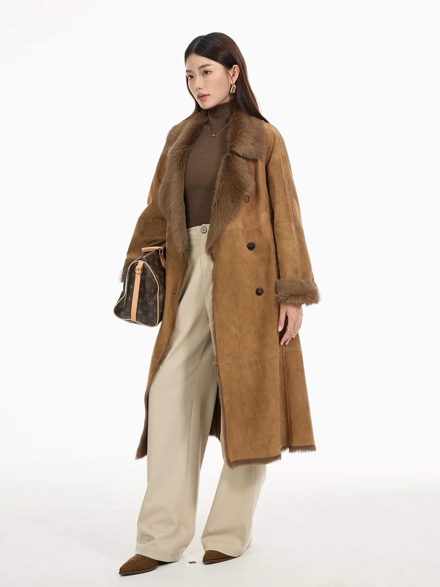 Model wearing the Golden Mist goatskin coat while holding a bag at hip level; belt tied, notch lapels slightly turned. — From Borcelleclothes.