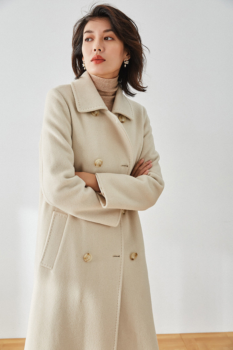 Moment of Promise beige coat, model with crossed arms showing the sharp shoulder line — From Borcelleclothes.