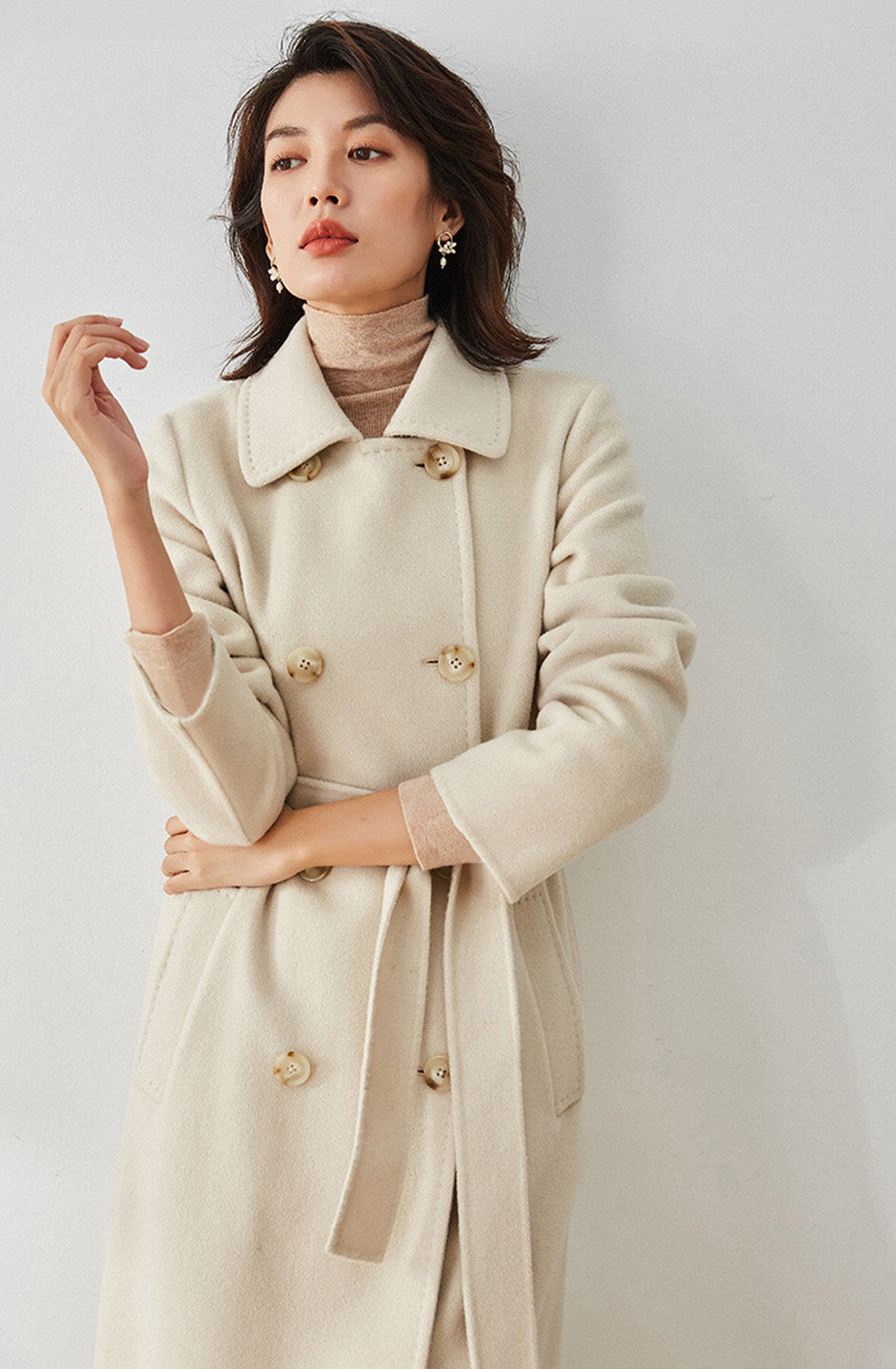 Moment of Promise beige coat, model with a raised arm showing the slim sleeve fit — From Borcelleclothes.