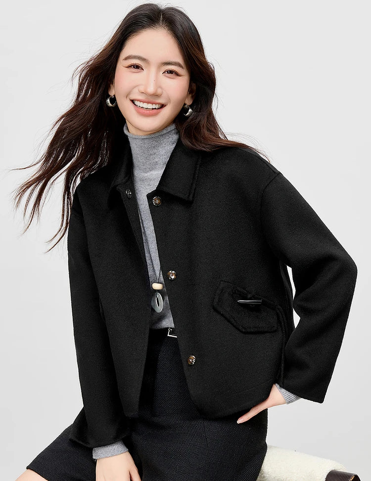 A seated woman in the Black Hellebore wool jacket with a hand on her hip, highlighting the jacket's fluid structure — From Borcelleclothes.