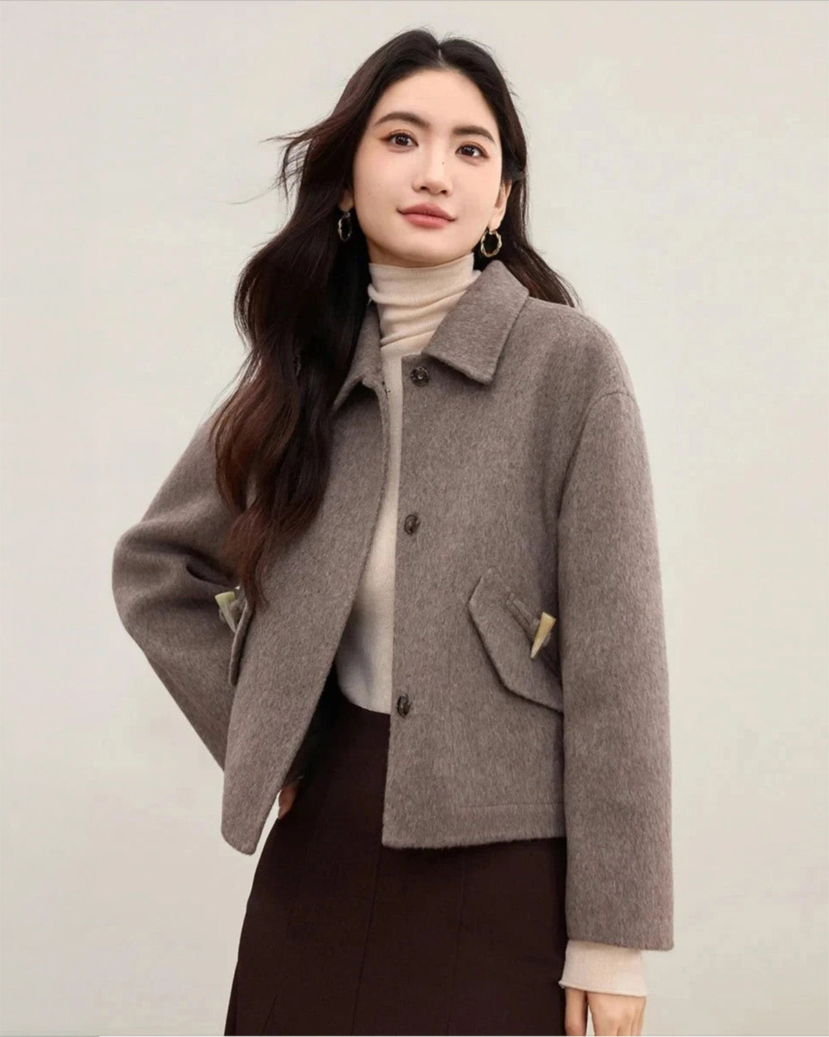A woman in the Lost Summit grey wool jacket with a hand on her hip, showing the signature toggle detail — From Borcelleclothes.