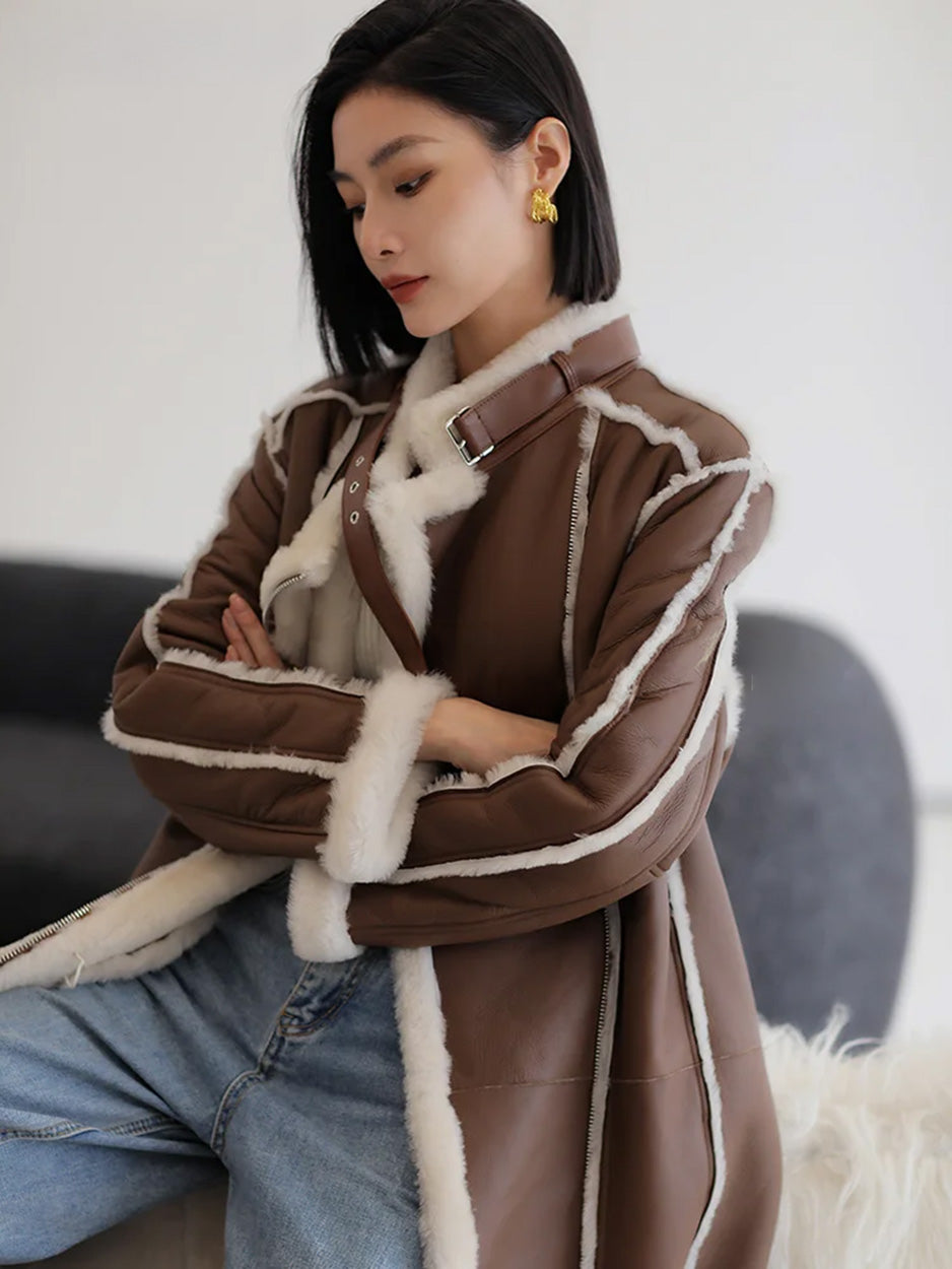 Seated model with crossed arms looking down, wrapped in the Drambuie Cocktail shearling coat — From Borcelleclothes.