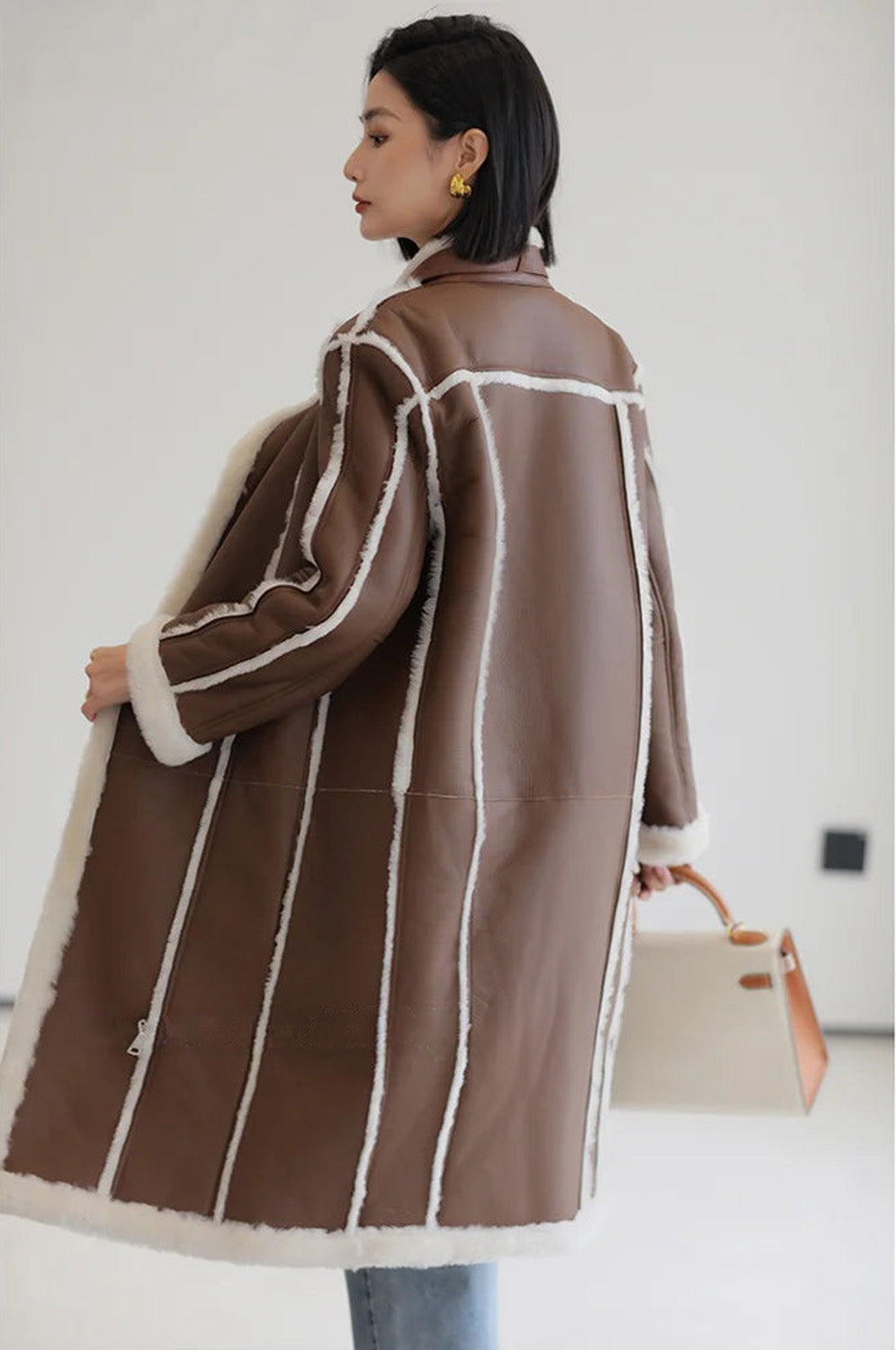 Back view of the Drambuie Cocktail shearling unzipped coat, model holding one edge — From Borcelleclothes.