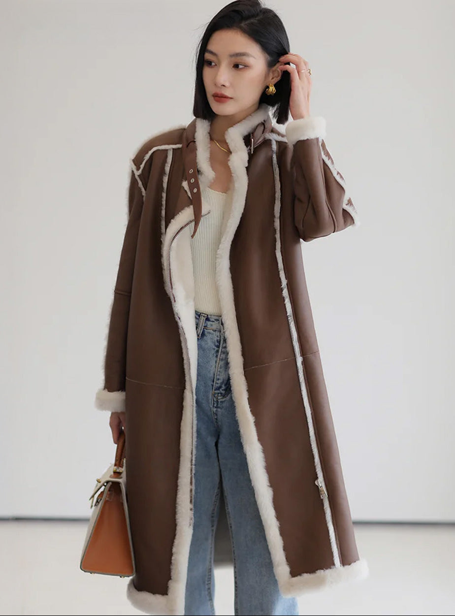 Women's mid-calf shearling coat in warm brown with exposed white fleece seams and asymmetrical zip closure, styled with relaxed elegance — From Borcelleclothes.