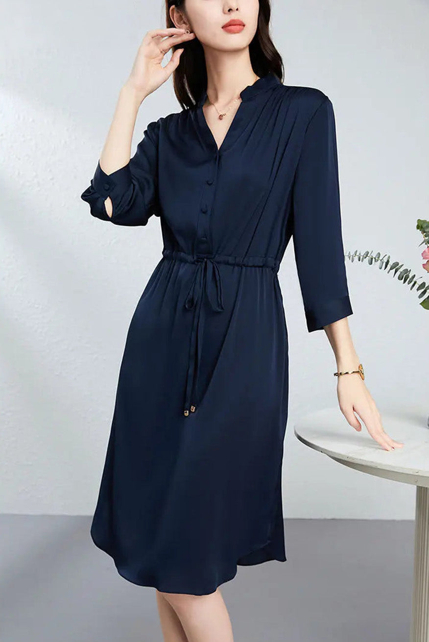 A woman showcasing the narrow stand-up collar and delicate silk-covered buttons of her dress while adjusting her earring. — From Borcelleclothes.