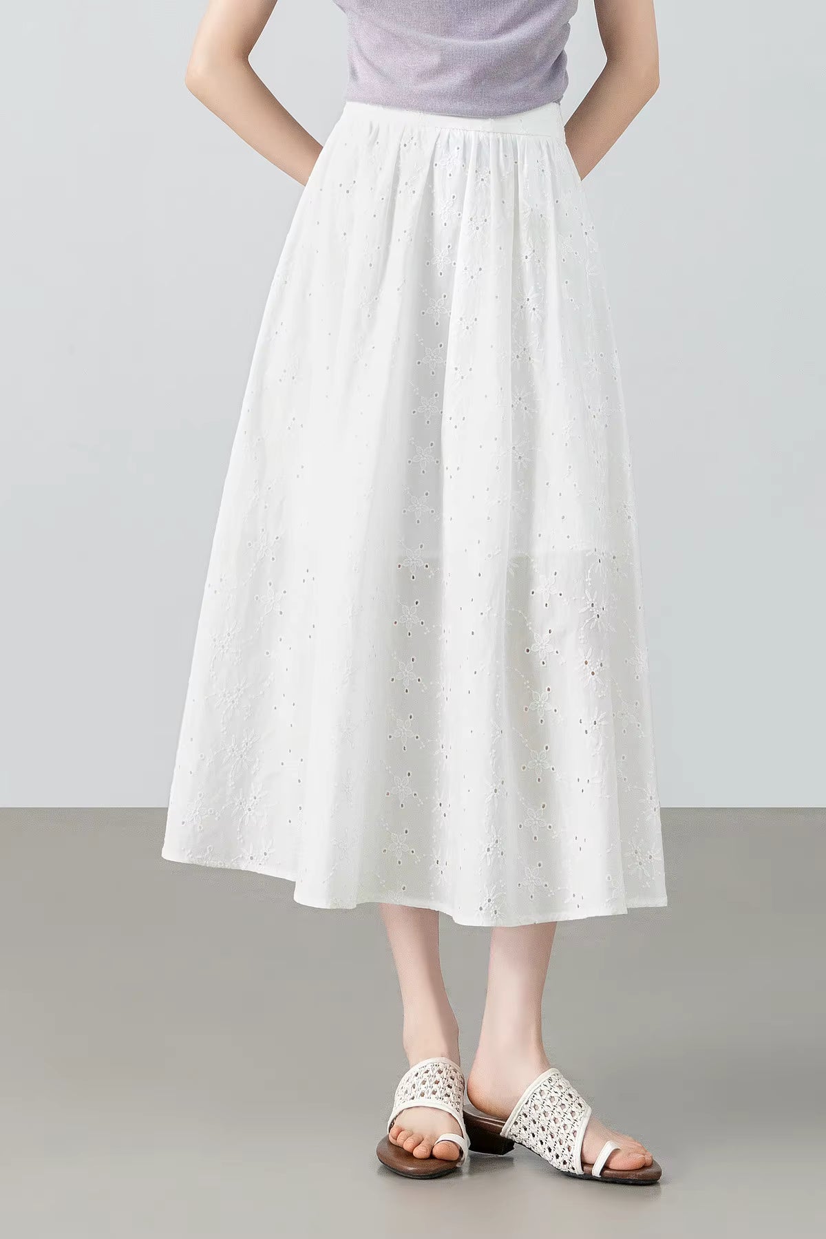 Full-length shot of a model posing from the front in a white embroidered eyelet cotton midi skirt with hands behind her back — From Borcelleclothes.