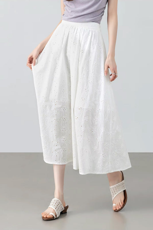 Front view of a model in motion wearing the white 100% cotton eyelet midi skirt, gently holding the fabric aside — From Borcelleclothes.