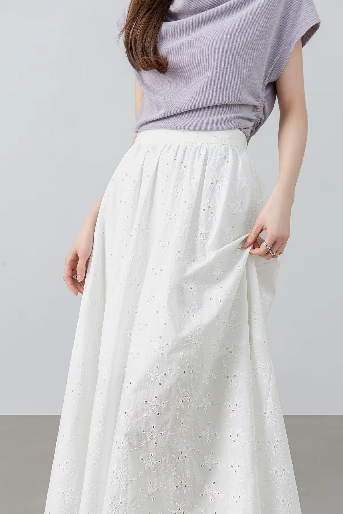 Side-angle view of a model turned slightly, holding the embroidered cotton fabric to demonstrate its lightweight texture — From Borcelleclothes.