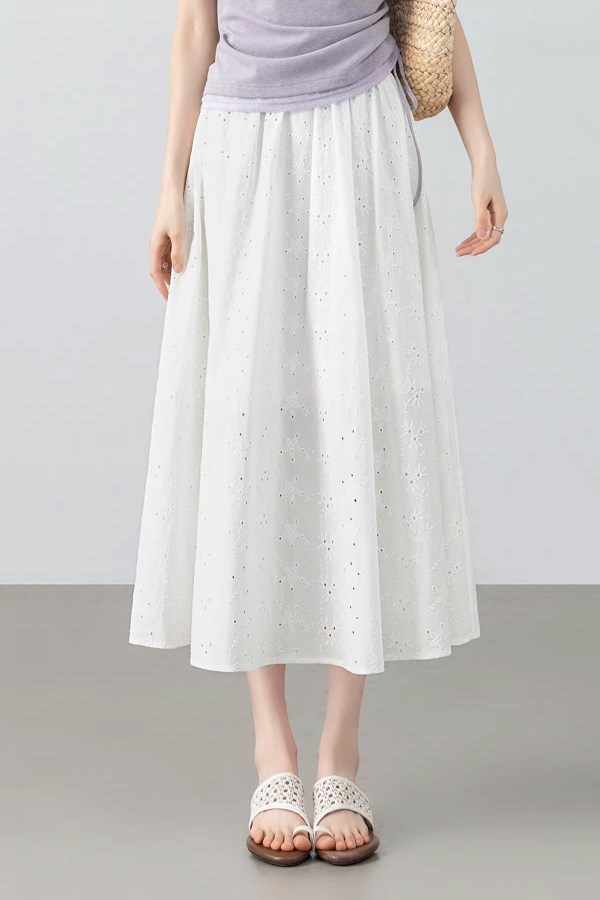 Summer lifestyle look featuring a model in a white cotton eyelet midi skirt holding a woven bag for a resort aesthetic — From Borcelleclothes.