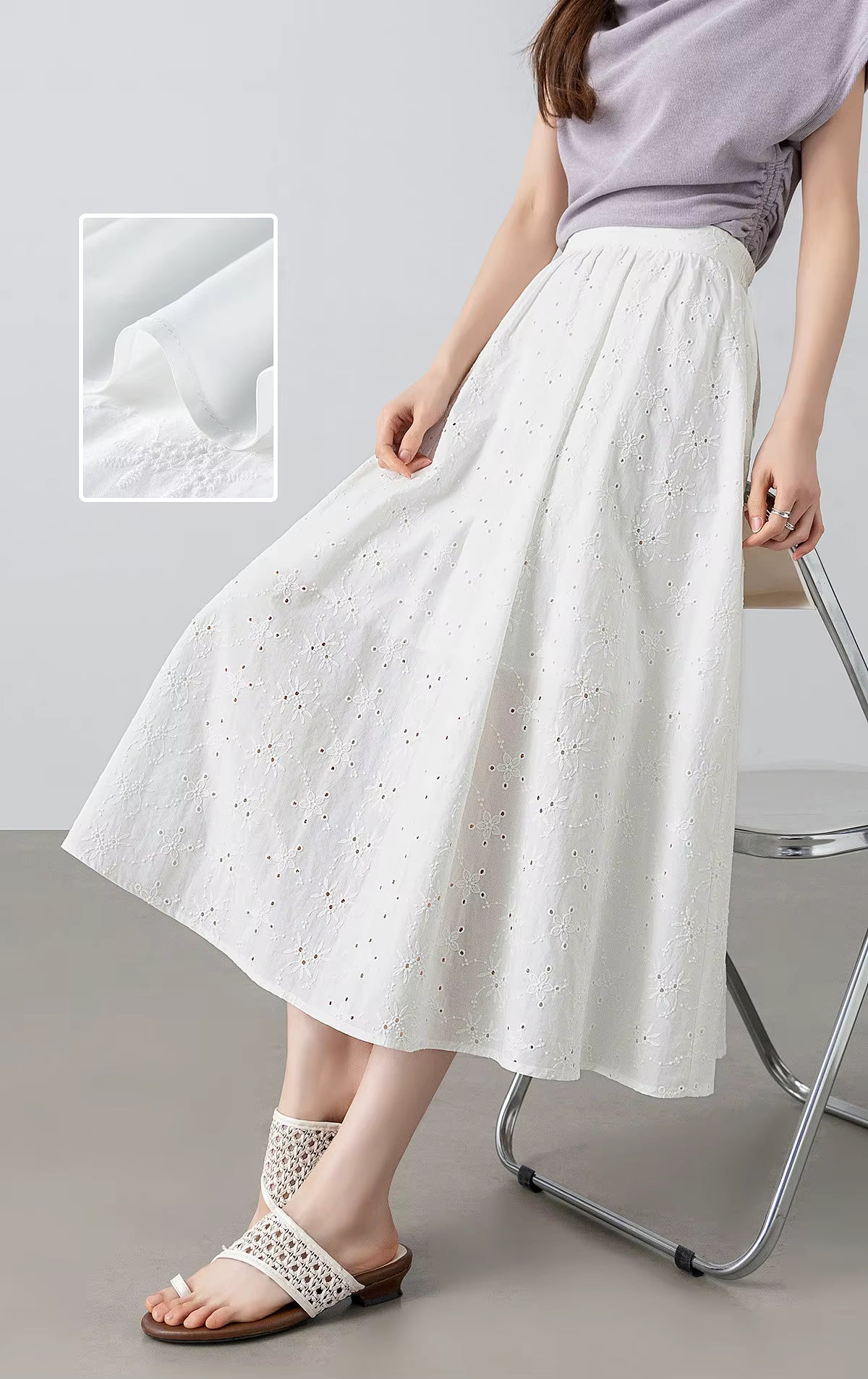 Elegant lifestyle shot of a model perching on the back of a chair, showcasing the relaxed drape of the white cotton eyelet skirt — From Borcelleclothes.