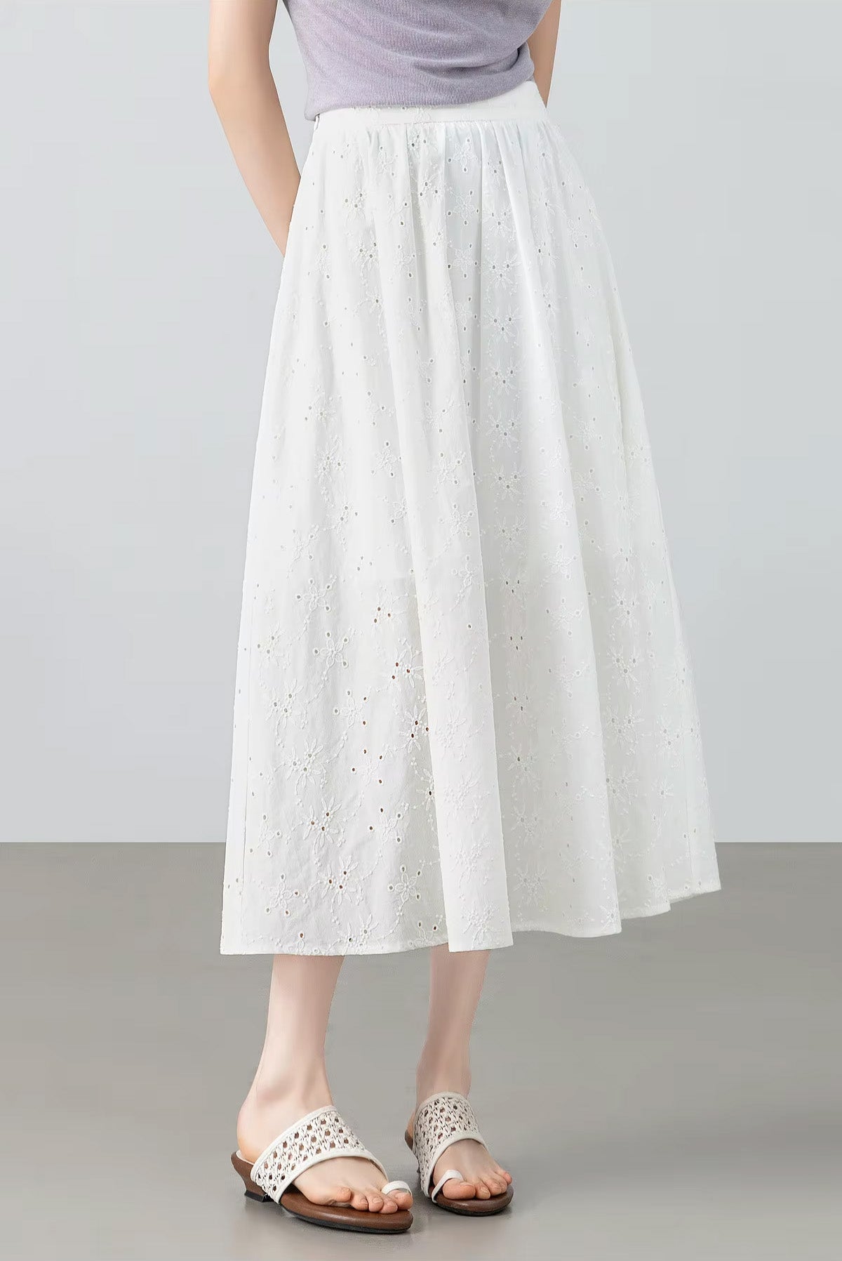 Three-quarter front view of a model turned slightly to the side, highlighting the flared silhouette of the white eyelet cotton skirt — From Borcelleclothes.