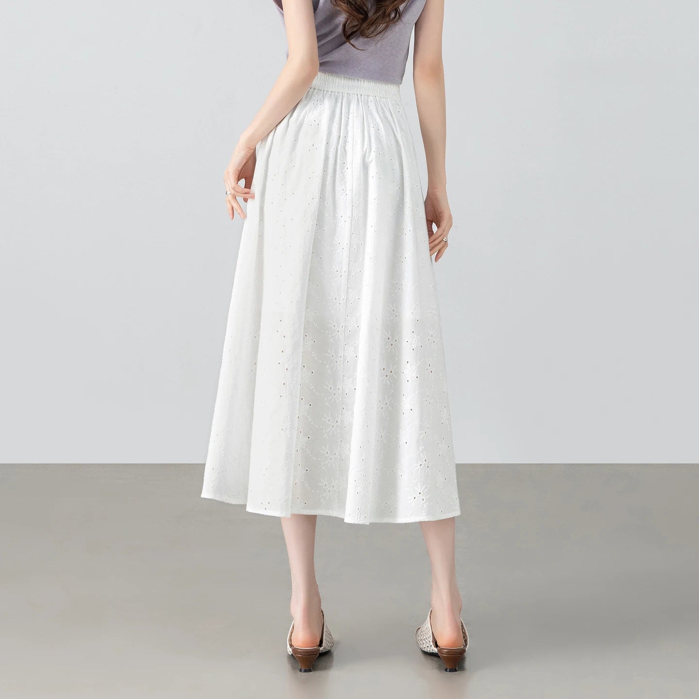 Studio pose focusing on the back profile of a model wearing the gathered white cotton eyelet summer skirt — From Borcelleclothes.