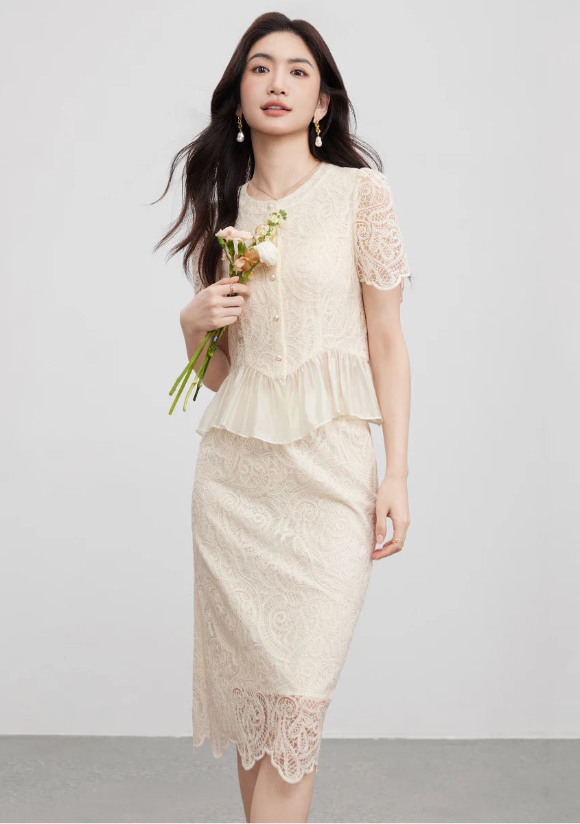 A woman holding a tousled bouquet near the pearl-buttoned bodice, blending the freshness of flowers with the lace. — From Borcelleclothes.
