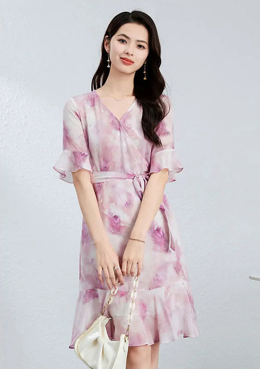 A woman in a flared silk wrap dress in Highland Heather, holding a white bag with both hands with calm confidence — From Borcelleclothes.