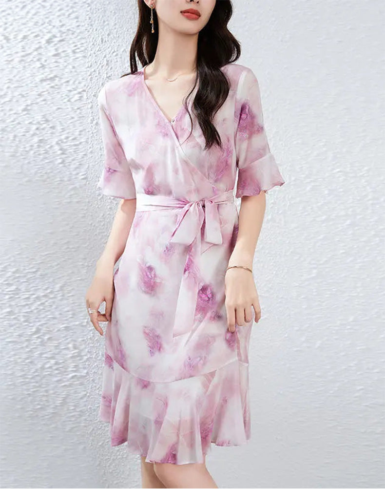 A woman gently lifting the skirt of her flared silk dress with both hands, letting the wind catch the wave-curved flounces — From Borcelleclothes.