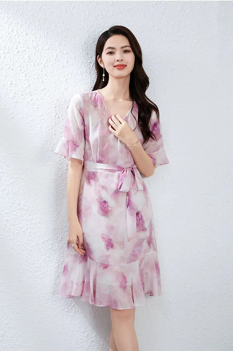 A woman thoughtfully touching the elegant V-neckline of her heather-purple silk dress — From Borcelleclothes.
