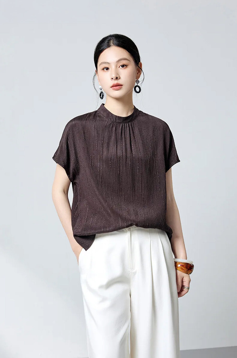 Model with hand in white pants pocket styled in espresso silk jacquard blouse by Borcelleclothes.