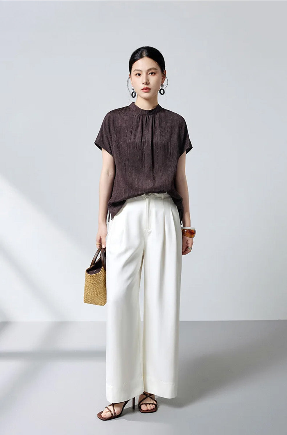 Model holding handbag looking forward in espresso silk blouse by Borcelleclothes.