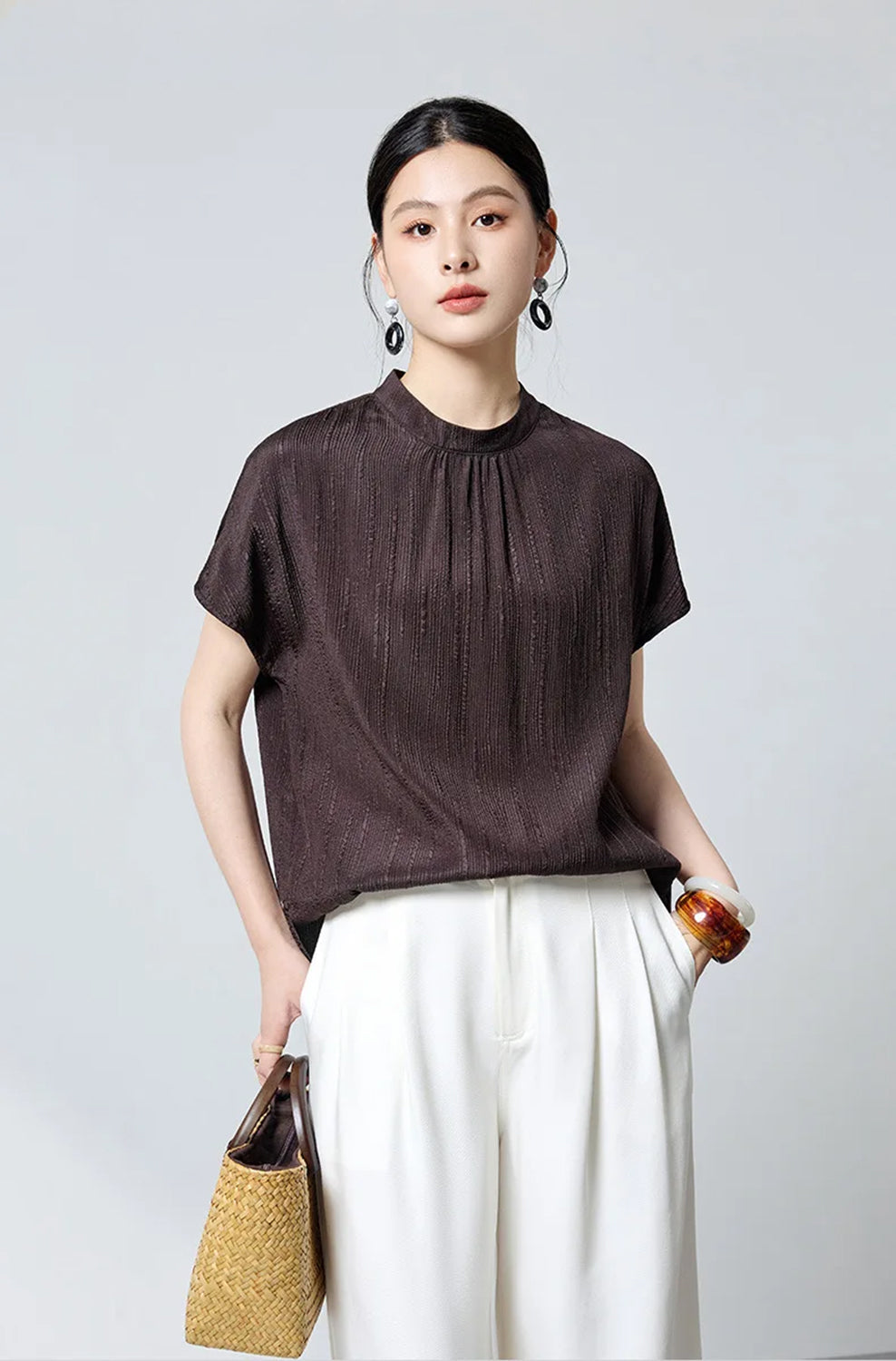 Model holding woven bag wearing brown fluted silk blouse by Borcelleclothes.
