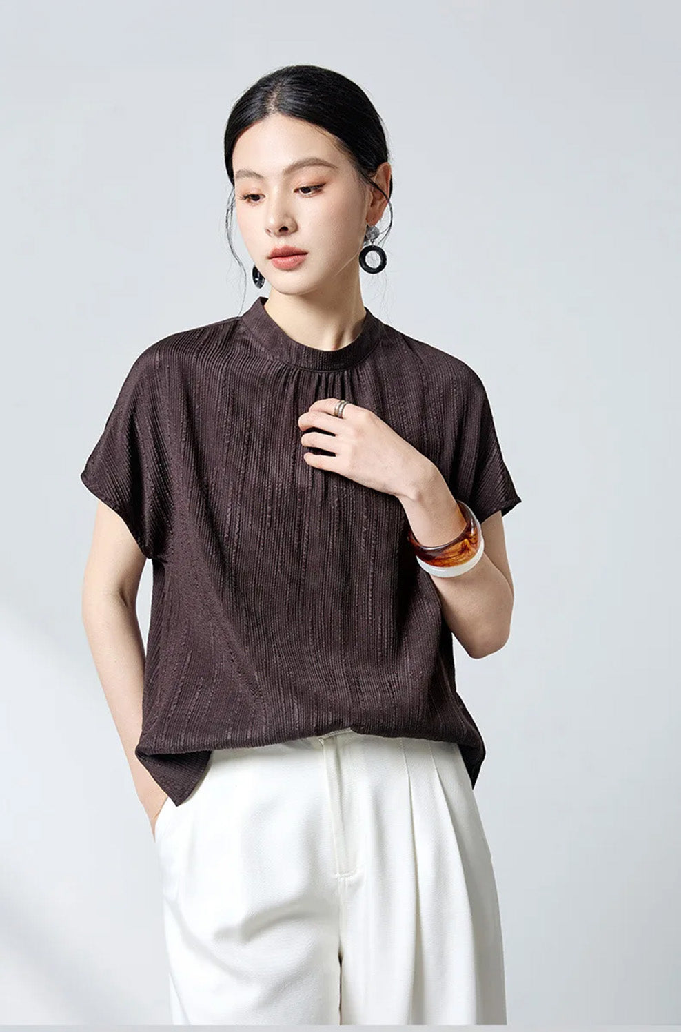 Model touching chest in dark espresso fluted jacquard silk blouse by Borcelleclothes.