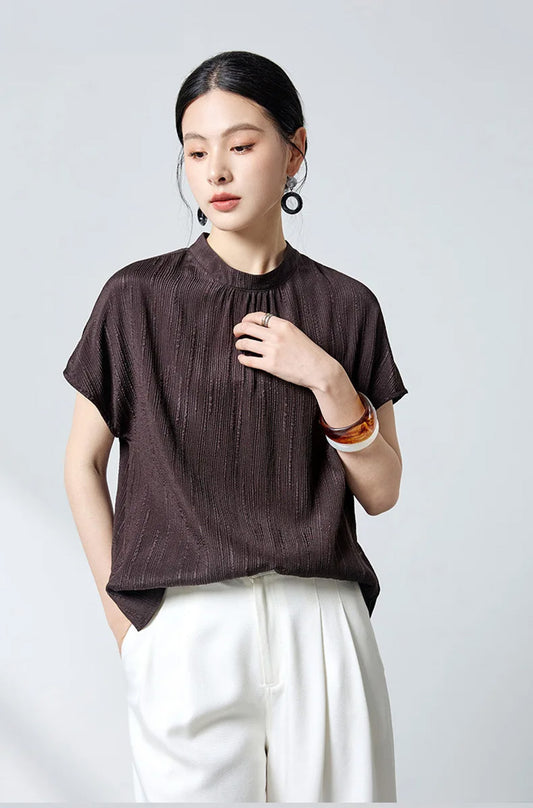 Model touching chest in dark espresso fluted jacquard silk blouse by Borcelleclothes.