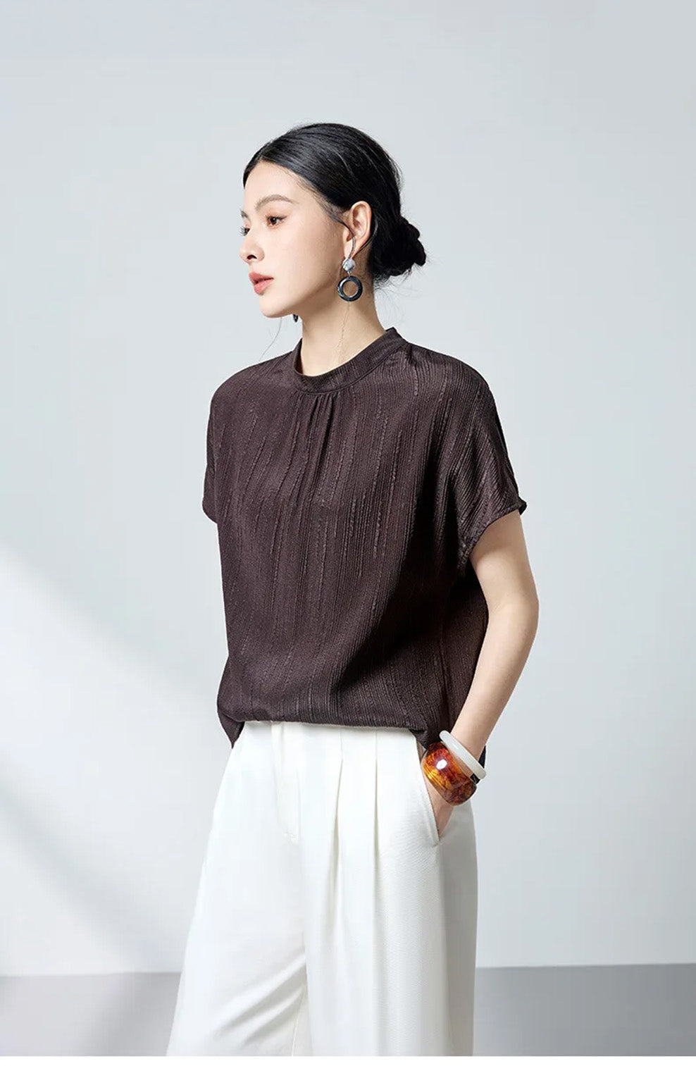 Three-quarter profile view of model wearing dark brown silk blouse by Borcelleclothes.