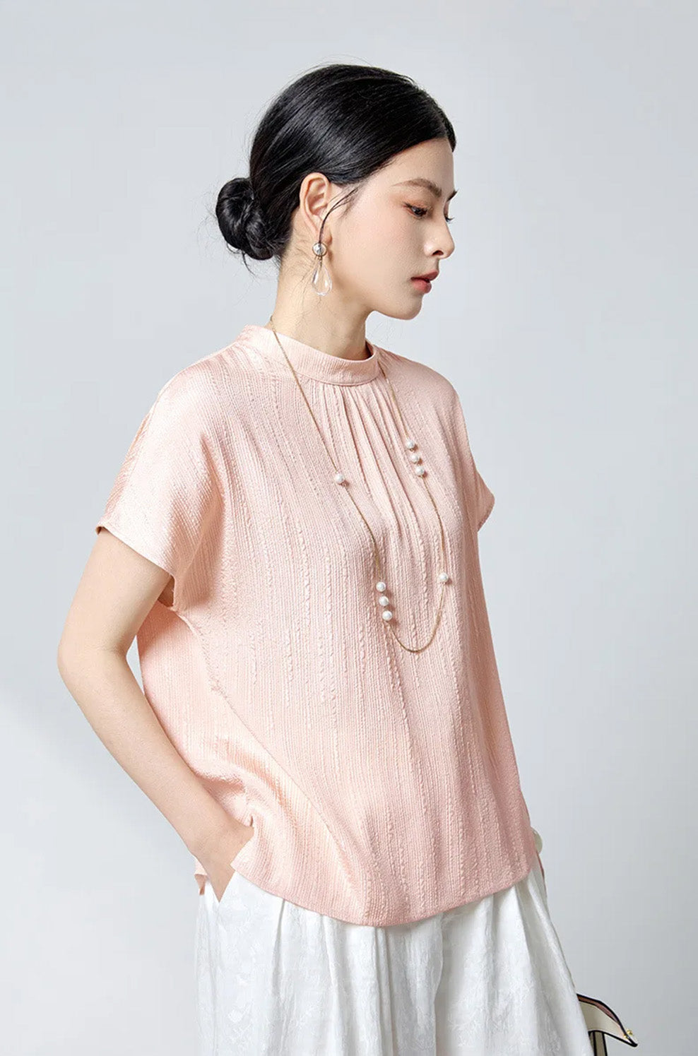 Model turned slightly side with hand in pocket wearing pink silk blouse by Borcelleclothes.