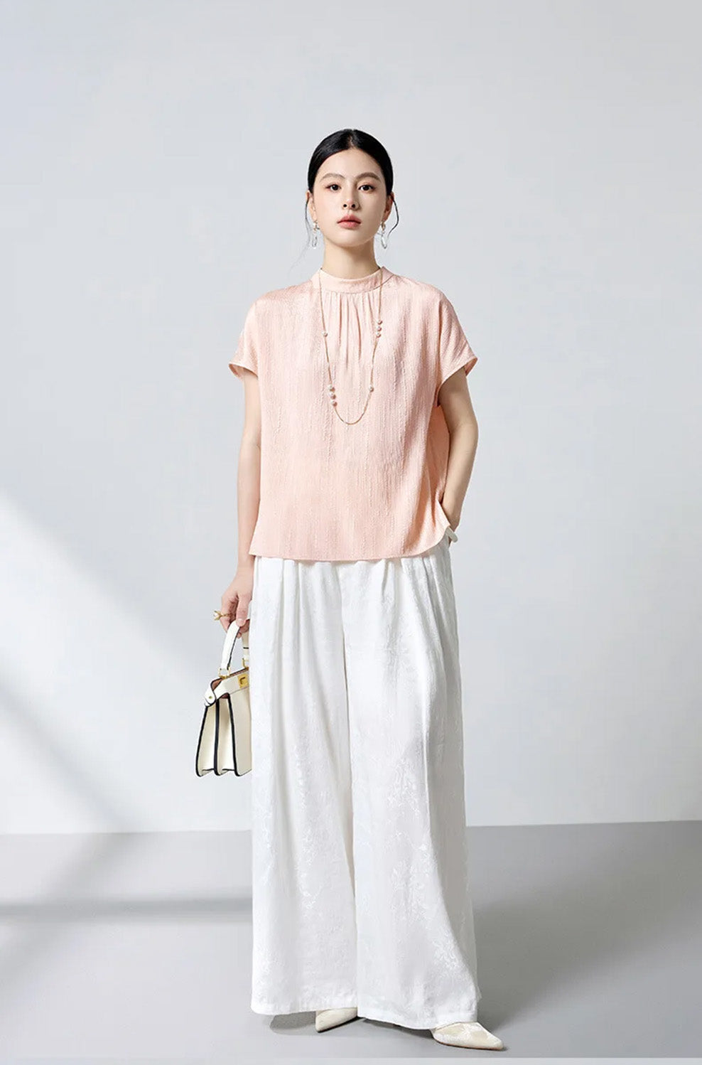 Model holding white handbag wearing pink textured jacquard silk blouse by Borcelleclothes.
