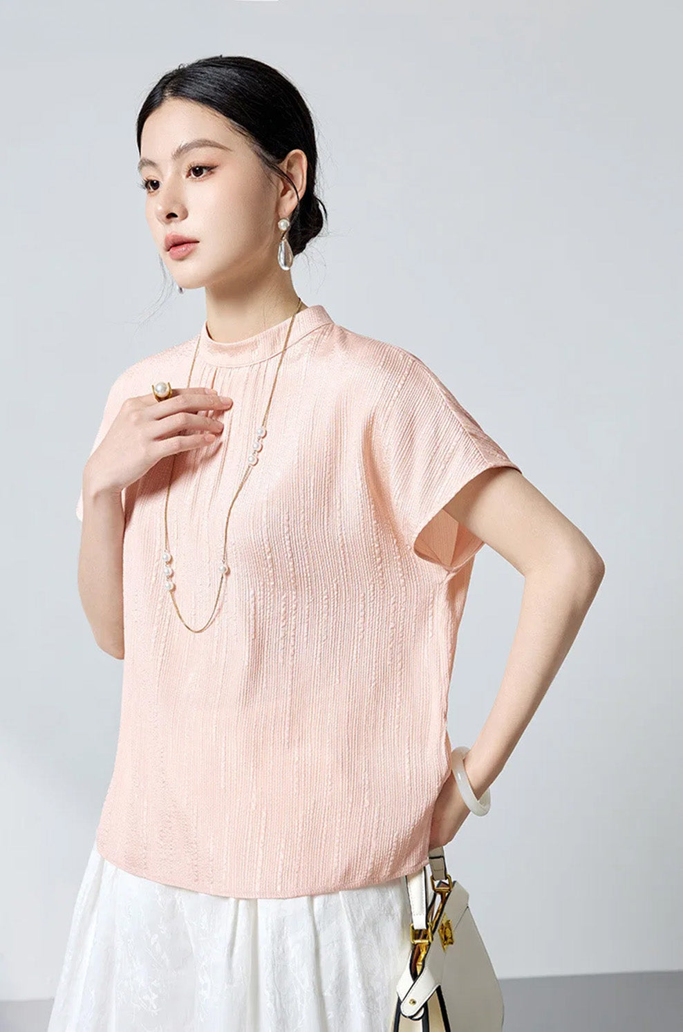 Model turned slightly side wearing blush pink fluted jacquard silk blouse by Borcelleclothes.