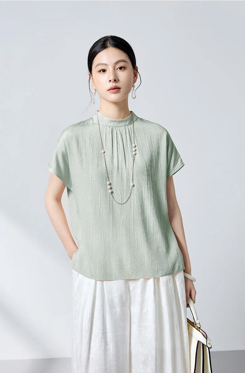Model styled with white bag wearing mint downpour fluted silk blouse by Borcelleclothes.