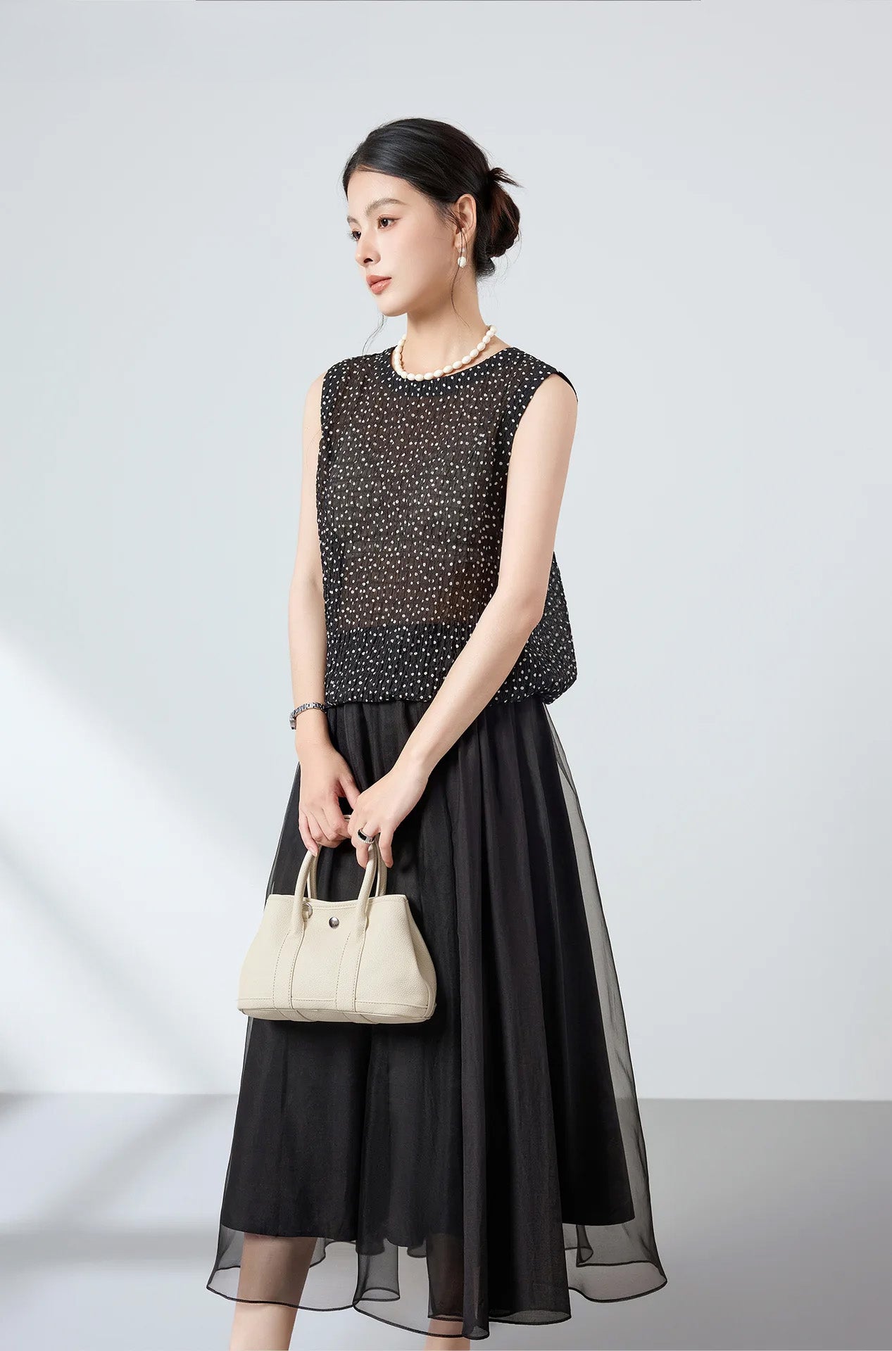 Model holding a bag with both hands wearing front-to-back silk blouse with clean front facade — From Borcelleclothes.