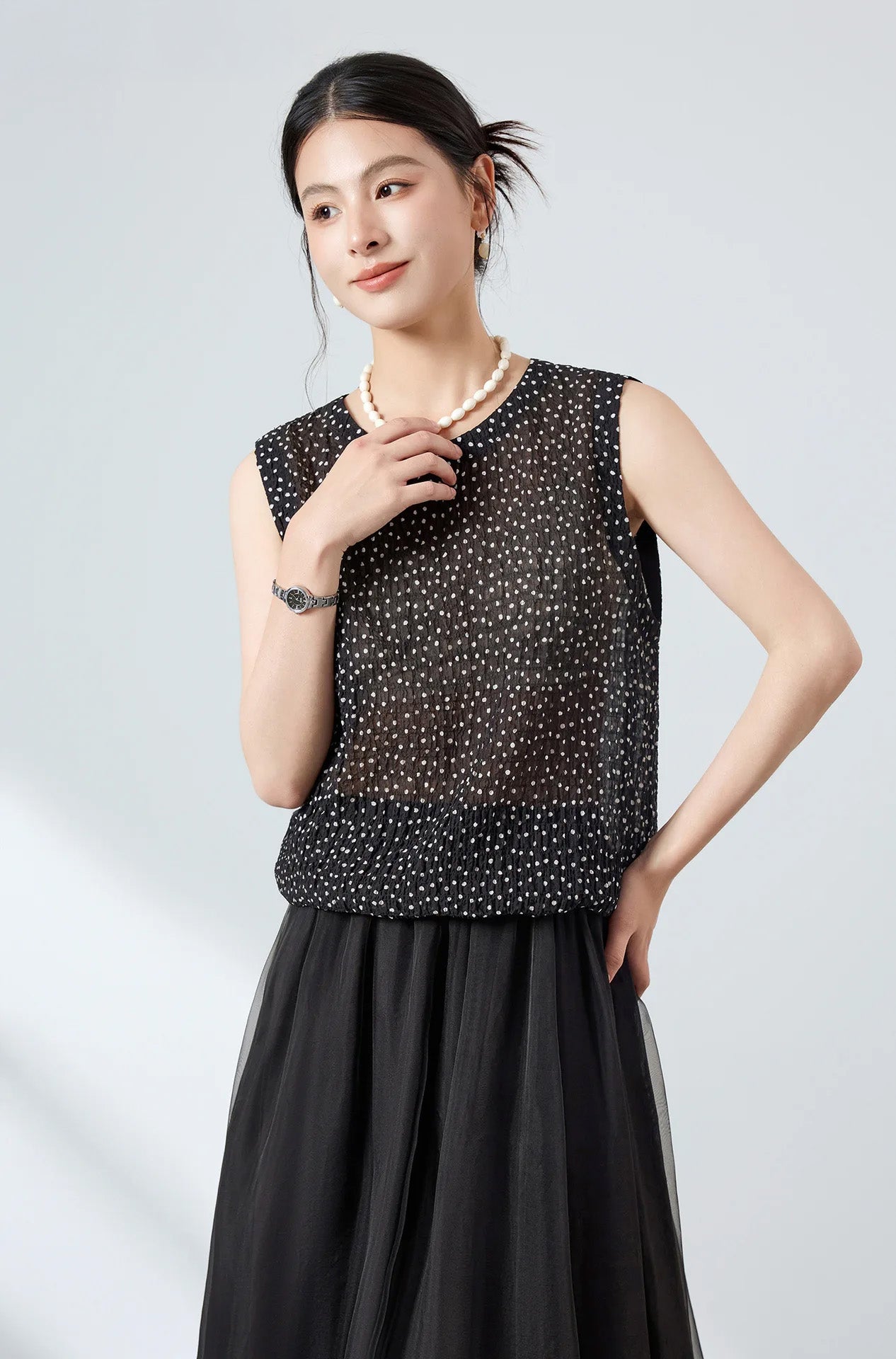 Model touching a pearl necklace wearing black front-to-back silk blouse with buttons at the back — From Borcelleclothes.