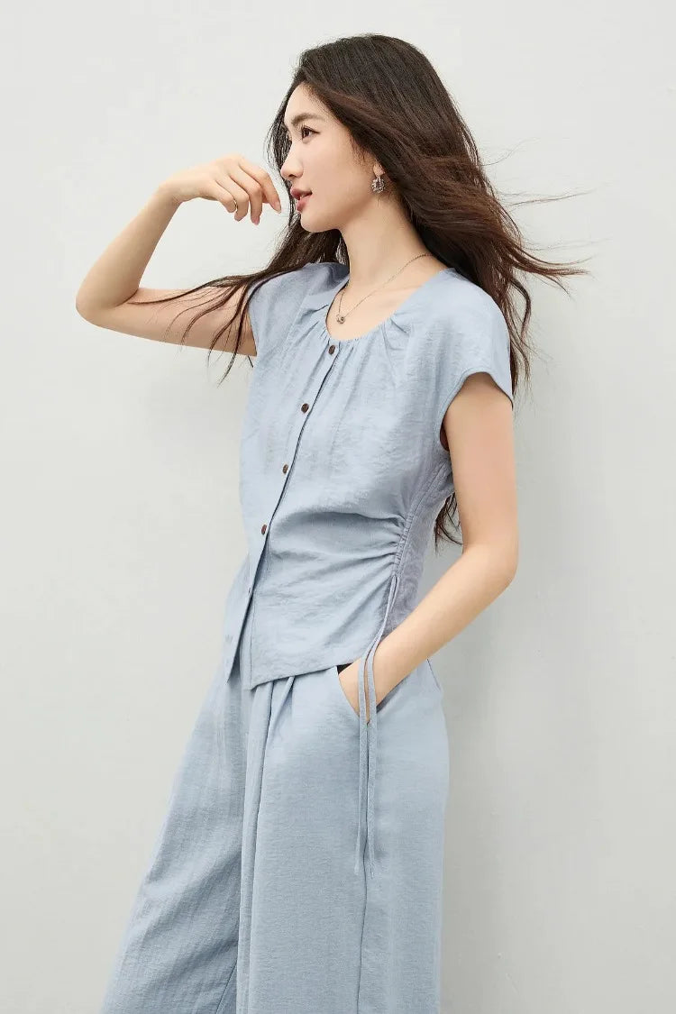 Side profile of a woman wearing the Bleu Soleil set, highlighting the high-low hem of the top and the volume of the trousers. — From Borcelleclothes.