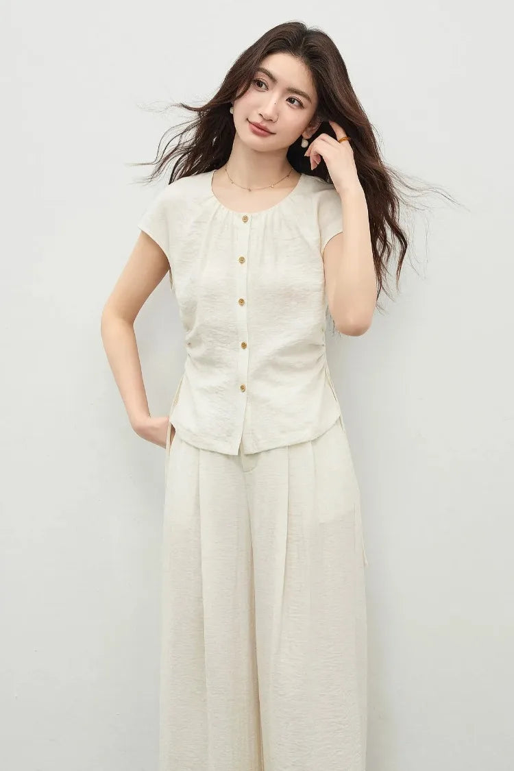 A woman in a soft marble-white crinkled viscose set, gently adjusting her hair to reveal the gathered neckline detail. — From Borcelleclothes.