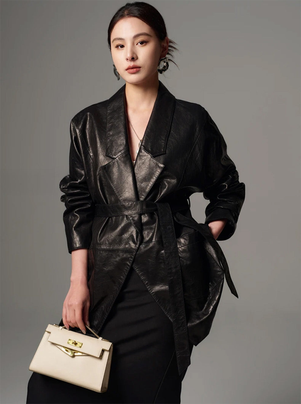 Three-quarter view of model with hand on hip holding a bag, styled in the Vola Con Me leather jacket — From Borcelleclothes.
