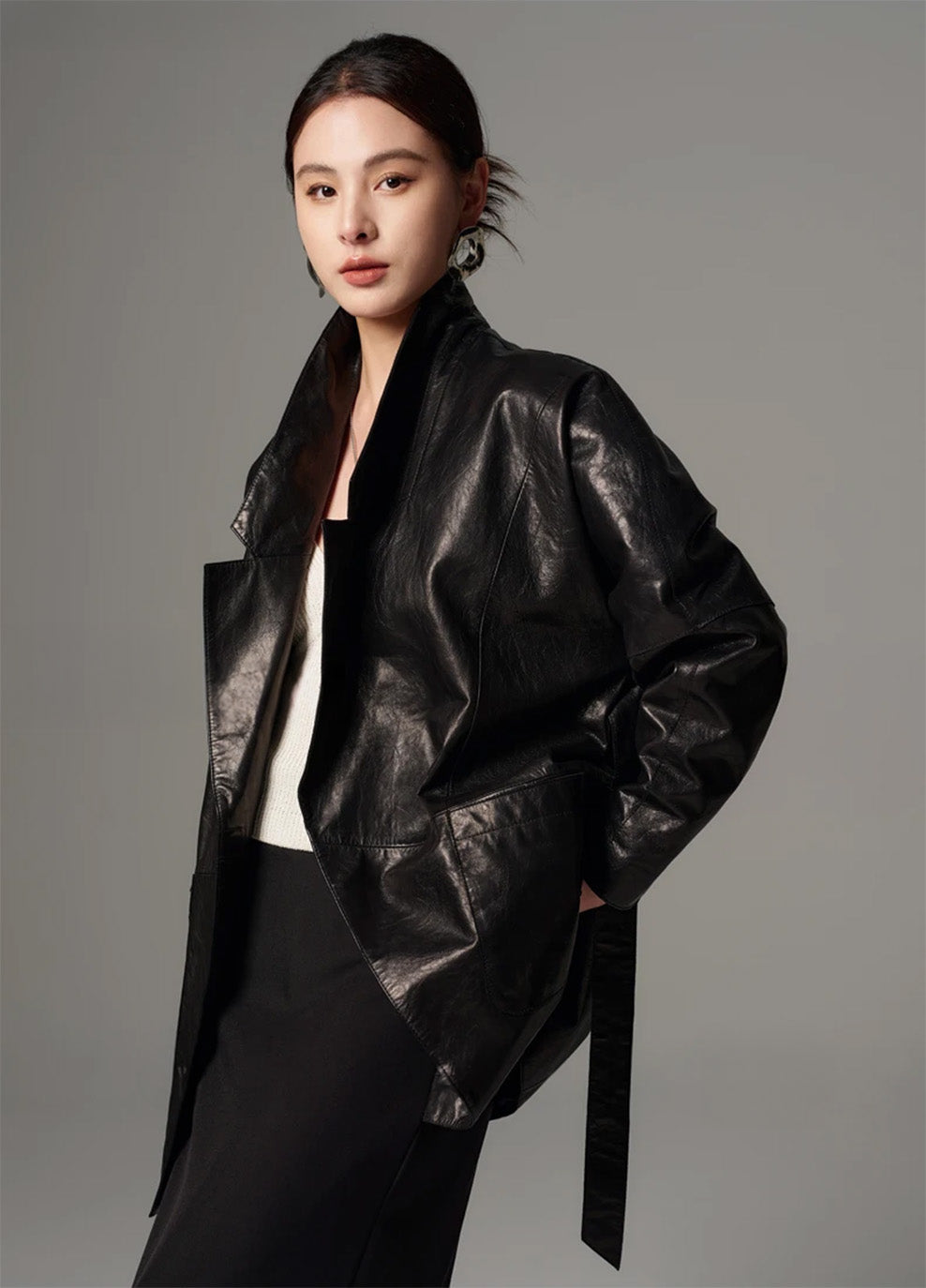 Model walking in the unfastened glazed leather wrap jacket with slightly lifted hem showing fluid movement — From Borcelleclothes.