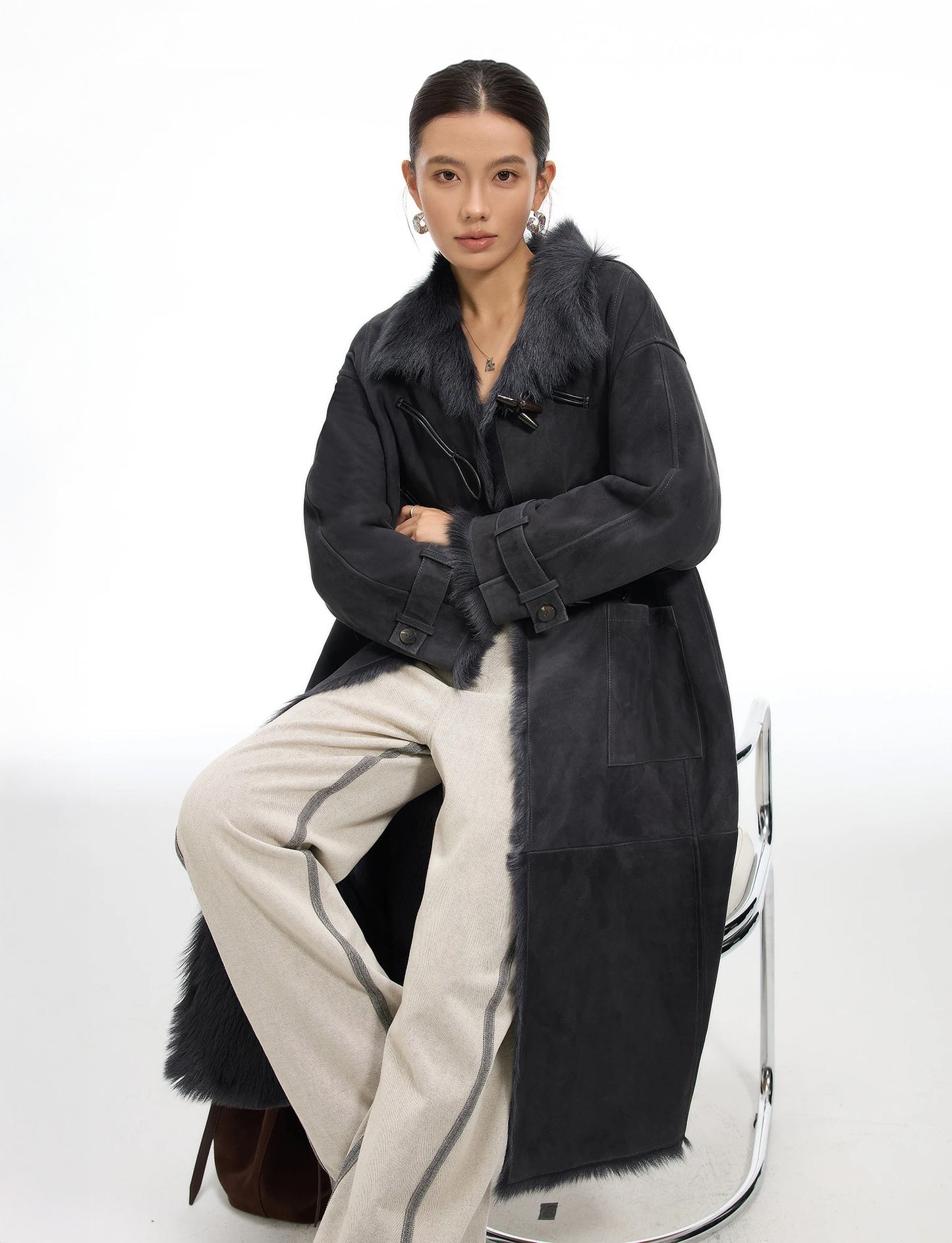 Model seated in Toscana goatskin coat, color Inner Depth; leather air loops and toggles visible at chest; Toscana fur along uncut hem — From Borcelleclothes.