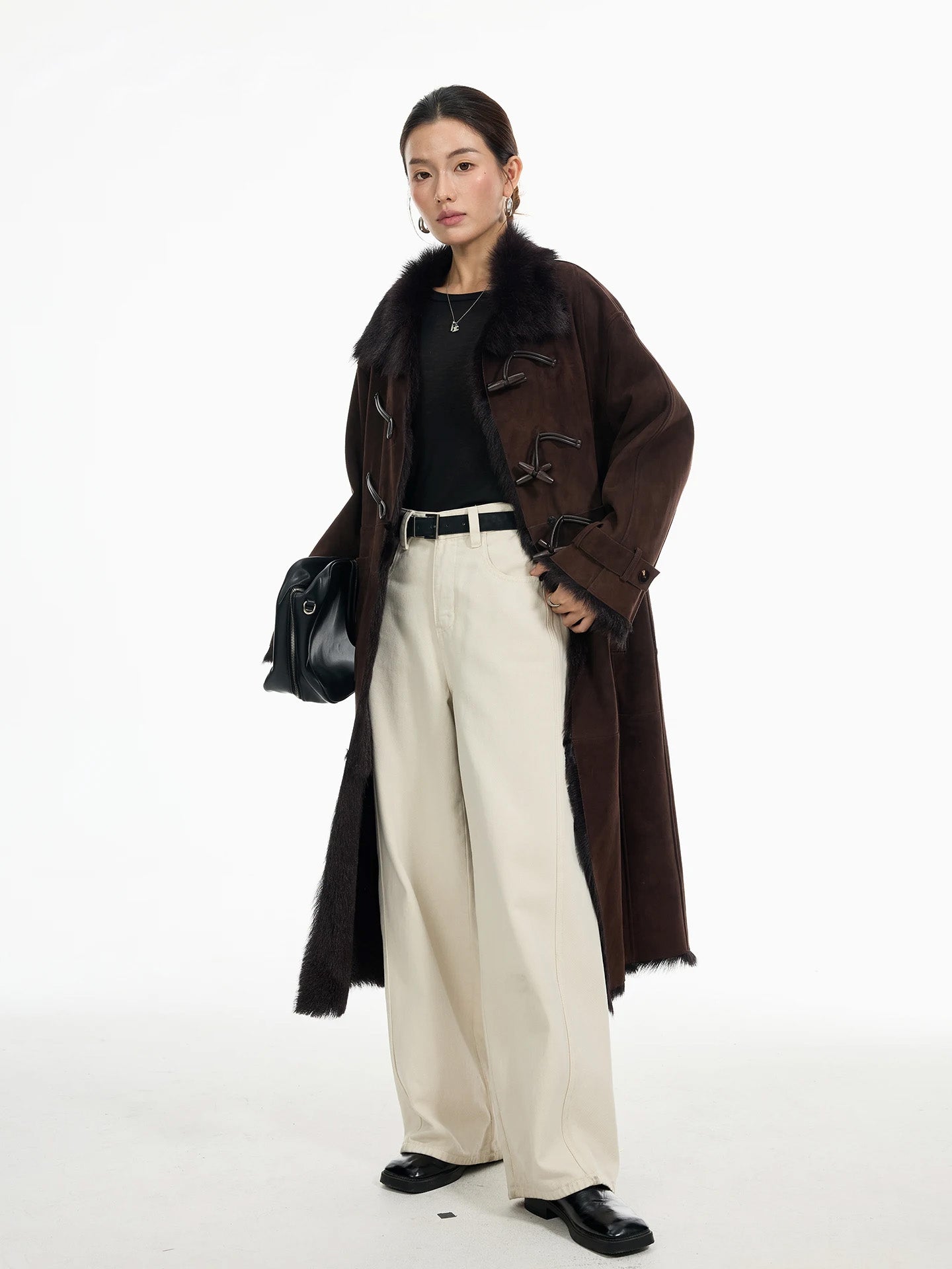 Model wearing goatskin coat in Wenge, holding bag at hip; leather air loops with toggle closure visible at chest; fur edges along hem — From Borcelleclothes.